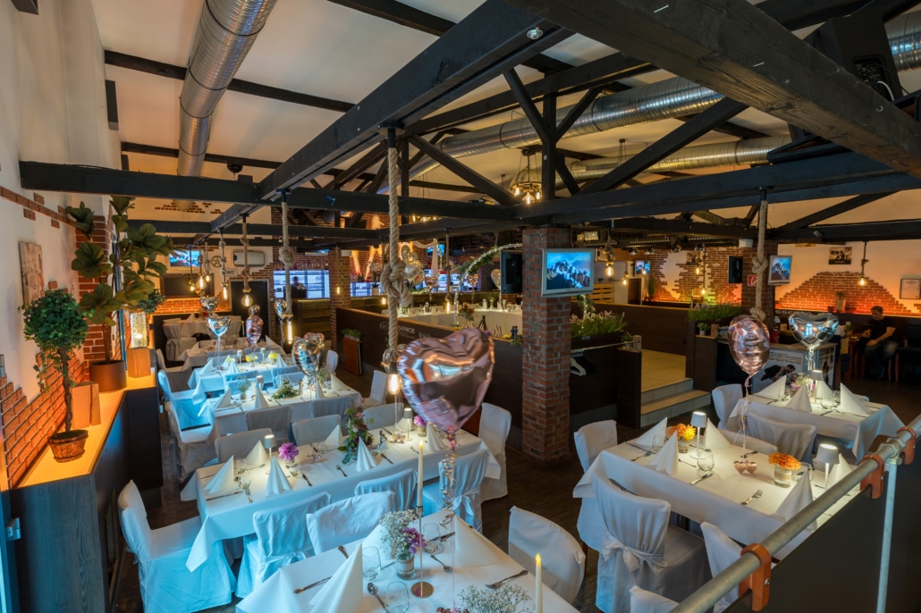 Panoramablick auf den modern-rustikalen Hochzeitssaal im Restaurant Essence in Hagen mit liebevoll dekorierten Tischen und festlicher Atmosphäre.