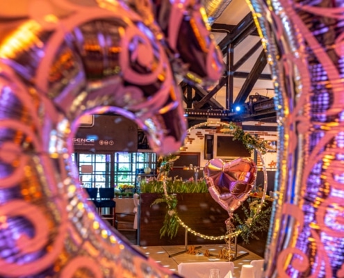 Blick durch dekorative Herzballons auf den festlich geschmückten Hochzeitssaal mit Herzballon und romantischer Dekoration im Restaurant Essence.